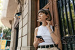 Incredible pretty woman with short stylish hair is holding smartphone and touching hair looking aside and rising outdoor