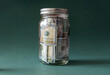 United States paper currency inside a glass jar piggy bank, green background.
