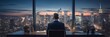 © Wolfilser - CEO manager sits in front of his desk in his office looking at the panorama of the illuminated skyline of a large city at night