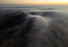 Soft Clouds Cascade Over The Darkened Landscape Of Fuerteventura As The First Light Of Sunrise Peeks Over The Horizon