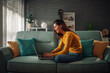 © Zamrznuti tonovi - Smiling woman using laptop and checking email while sitting on the couch at home
