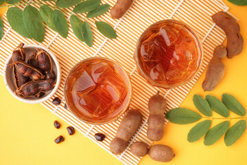 Glasses of tasty tamarind drink and fruits on yellow background