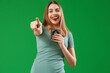 Laughing young woman with Koran pointing at viewer on green background. Accusation concept