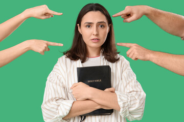 Wall Mural - People pointing at young woman with Holy Bible on green background. Accusation concept