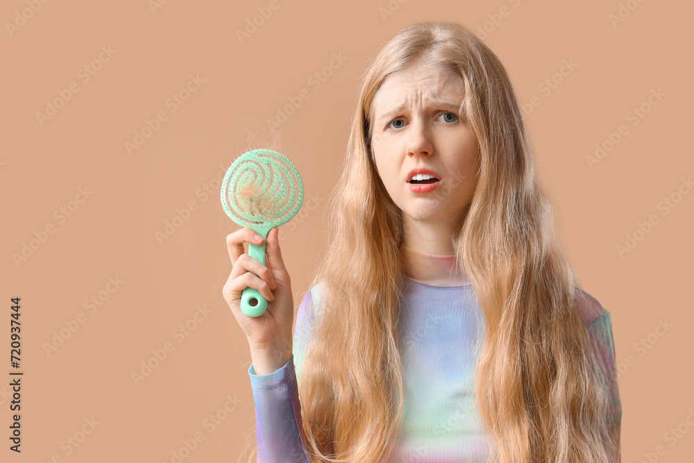 Young woman with hair loss problem and brush on beige background