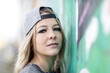 A young blond woman posing in front of a graffity wall outdoors