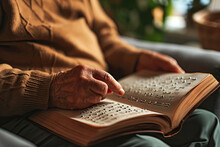 Blind Senior Person Reading Book Written In Braille On Sofa Indoors, Closeup