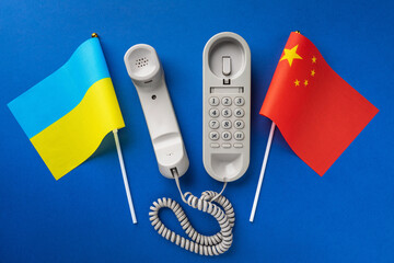 Top view of an old telephone and two flags on a blue background, concept on the theme of telephone conversations between Ukraine and China