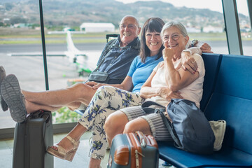 Canvas Print - Smiling group of senior friends sitting in airport departure area waiting for boarding. Travel and tourism concept, retiree lifestyle