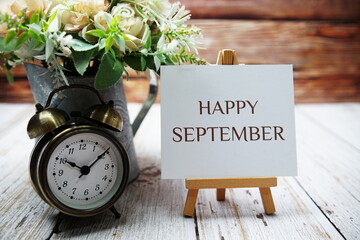 Canvas Print - Happy September text message written on paper card with wooden easel and alarm clock with flower in metal vase decoration