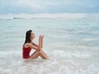 © SHOTPRIME STUDIO - Woman with a beautiful tan tourist in a red swimsuit sitting on the sand on the beach in the ocean in the waves pensive