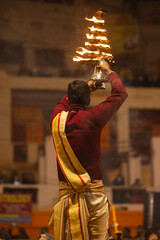 Wall Mural - Ganga aarti, Portrait of young priest performing holy river ganges evening aarti at dashashwamedh ghat in traditional dress with hindu rituals.	
