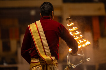 Wall Mural - Ganga aarti, Portrait of young priest performing holy river ganges evening aarti at dashashwamedh ghat in traditional dress with hindu rituals.	