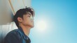 © NickArt - Profile headshot of young korean model looking stylish man leaning on the street wall on sunny day with head up tired or posing and clear blue sky copyspace background