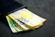 Euro banknotes inside a black wallet on a black background,