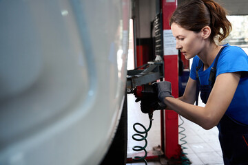 Wall Mural - Woman auto mechanic removes a car wheel on car lift