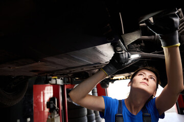 Wall Mural - Young repair technician inspecting the underbody of a car