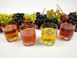 Drinking glasses with grape juice of different varieties stand in a row on a white table against the background of bunches of fresh ripe grapes.
