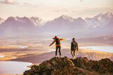 Fototapeta  - Young couple of hikers with backpacks is walking at mountain top with great view