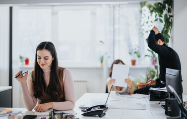 Wall Mural - Focused woman at work with colleagues in a bright office, conveying teamwork and productivity.