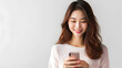 © BeautyStock - happy smiling pretty asian woman holding mobile phone looking at smartphone, typing, doing ecommerce online shopping on cell isolated on studio white background, communication technology concept