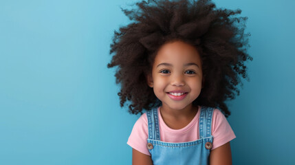 Wall Mural - young African American girl with a big smile, wearing a pink shirt and a blue denim jumper, set against a light blue background