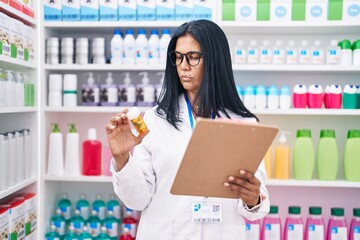 Wall Mural - Middle age hispanic woman pharmacist holding pills bottle reading document at pharmacy