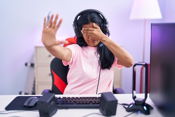 Sticker - Mature hispanic woman playing video games at home covering eyes with hands and doing stop gesture with sad and fear expression. embarrassed and negative concept.