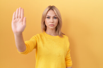 Canvas Print - Young caucasian woman wearing yellow sweater doing stop sing with palm of the hand. warning expression with negative and serious gesture on the face.