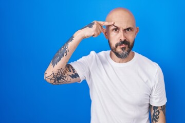 Sticker - Hispanic man with tattoos standing over blue background pointing unhappy to pimple on forehead, ugly infection of blackhead. acne and skin problem