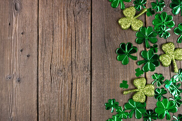 Wall Mural - St Patricks Day side border of  shiny shamrocks. Overhead view over a rustic dark wood background with copy space.