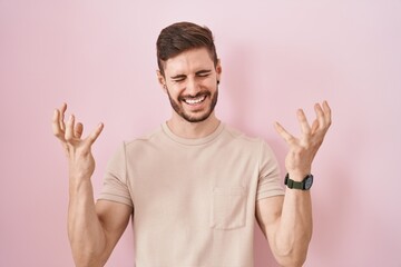 Poster - Hispanic man with beard standing over pink background celebrating mad and crazy for success with arms raised and closed eyes screaming excited. winner concept