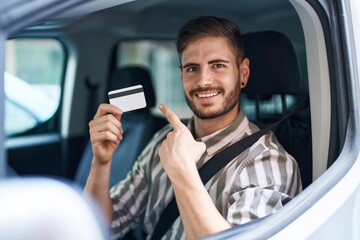 Poster - Hispanic man with beard driving car holding credit card smiling happy pointing with hand and finger