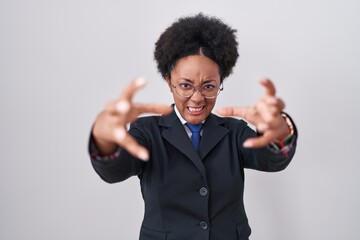 Wall Mural - Beautiful african woman with curly hair wearing business jacket and glasses shouting frustrated with rage, hands trying to strangle, yelling mad