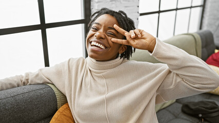 Poster - A joyful african american woman with dreadlocks posing playfully in a cozy living room setting.