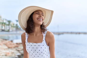 Wall Mural - Young african american woman wearing summer hat looking to the side at seaside