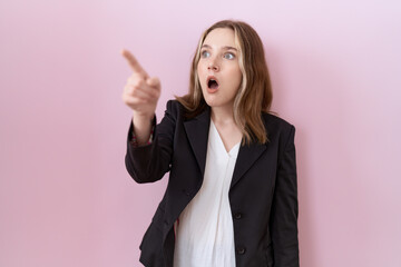 Wall Mural - Young caucasian business woman wearing black jacket pointing with finger surprised ahead, open mouth amazed expression, something on the front