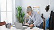 © Krakenimages.com - Mature woman with grey hair working in a modern office, standing at her desk with papers and a laptop.