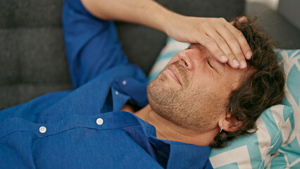 Sticker - Young hispanic man suffering for headache lying on sofa at home