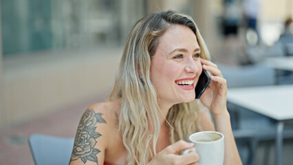 Wall Mural - Young blonde woman talking on smartphone drinking coffee at coffee shop terrace