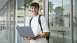 © Krakenimages.com - Cheerful hispanic teenager at university, a young, smart student enjoying laptop studies in the sunlight, backpack slung over a casual outfit.