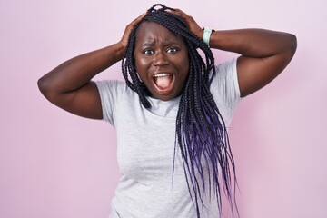 Wall Mural - Young african woman standing over pink background crazy and scared with hands on head, afraid and surprised of shock with open mouth