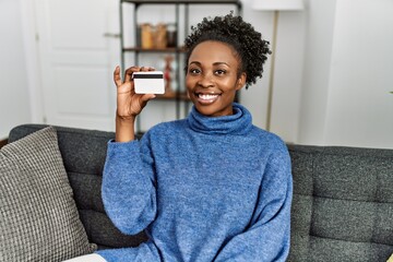 Poster - African american woman holding credit card sitting on sofa at home