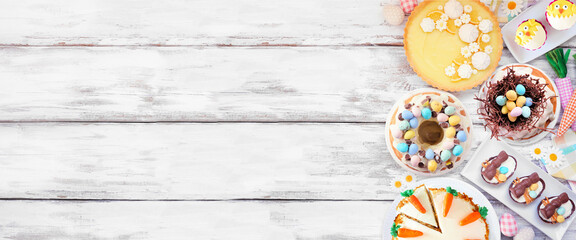 Wall Mural - Easter or spring dessert food side border. Top view over a white wood banner background. Lemon tart, cupcakes, Easter egg and carrot cakes and an assortment of sweets. Copy space.