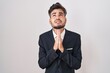 © Krakenimages.com - Young hispanic man with tattoos wearing business suit and tie begging and praying with hands together with hope expression on face very emotional and worried. begging.