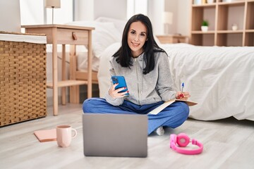 Poster - Young caucasian woman student writing on book using smartphone at bedroom