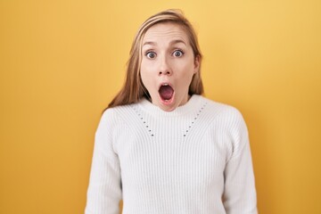 Poster - Young caucasian woman wearing white sweater over yellow background afraid and shocked with surprise and amazed expression, fear and excited face.