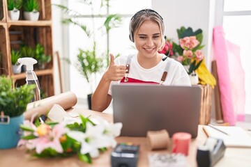 Canvas Print - Young blonde woman working at florist shop doing video call smiling happy and positive, thumb up doing excellent and approval sign