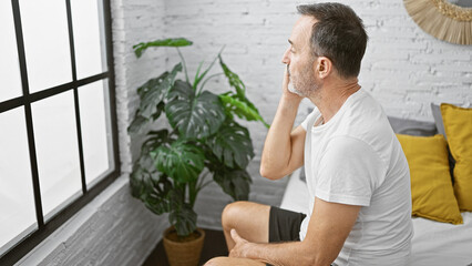 Wall Mural - Middle age man with grey hair sitting on bed looking throw the window at bedroom