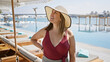 A smiling woman in a sunhat enjoys a luxurious poolside ambiance at a tropical resort overlooking the sea.